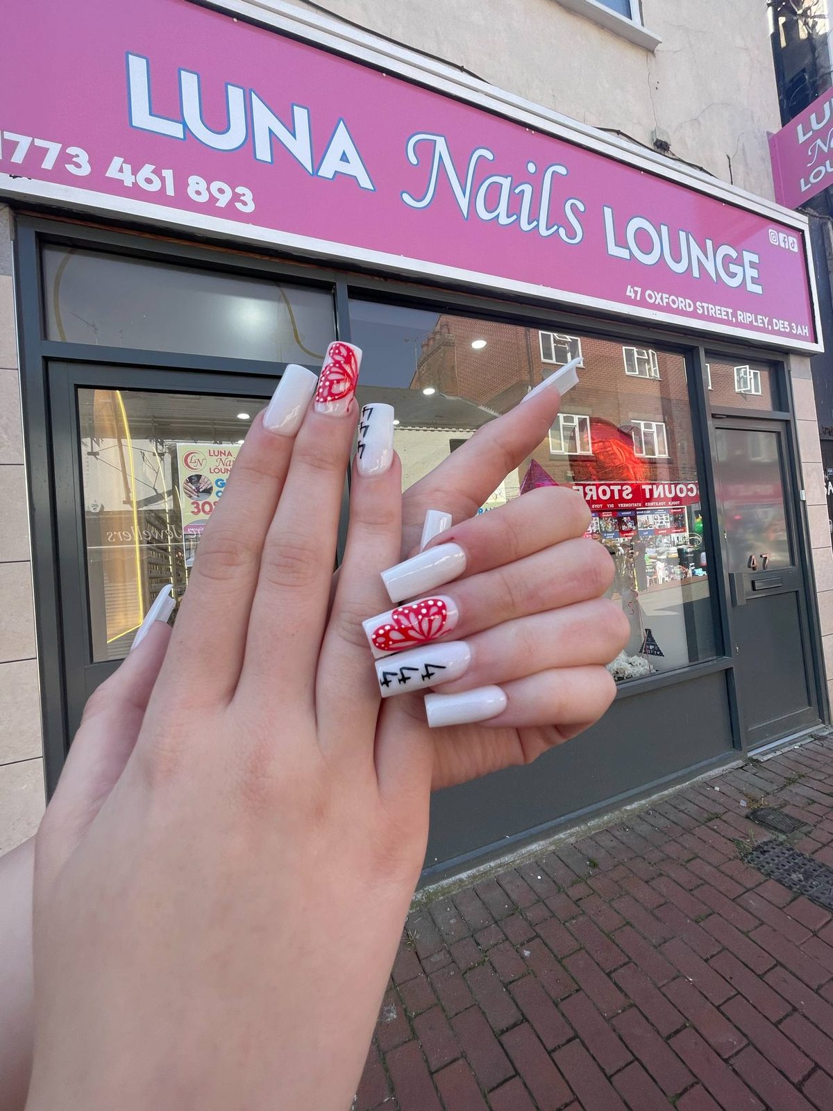 White nails with red floral art held up in front of the pink shop sign