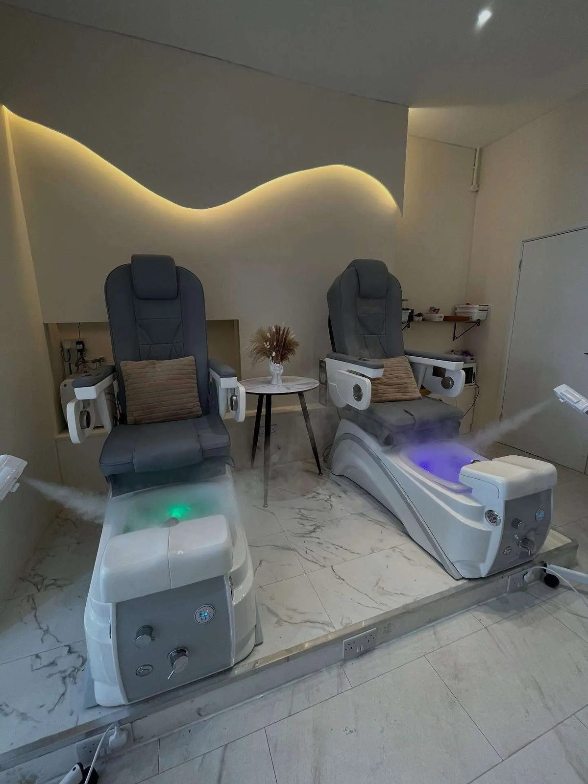 Two pedicure chairs with foot spas under a curved lit wall