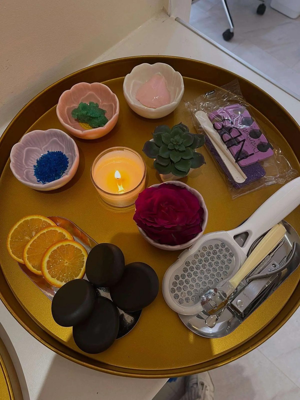 A herbal pedicure tray with orange slices, a candle, hot stones, a rose and herbs